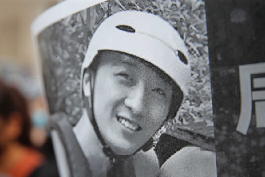 A protester holds up a black and white image of Chow Tsz-Lok, who is smiling and wearing a helmet