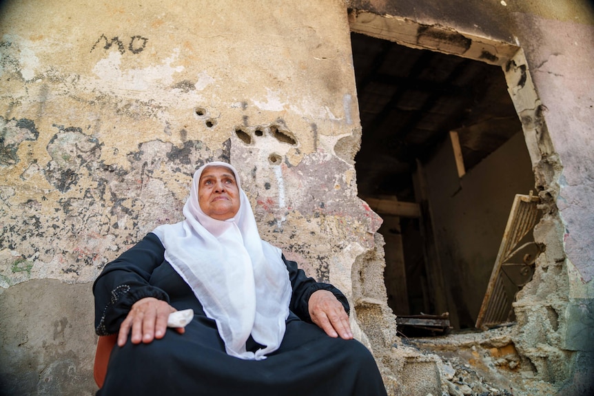 A woman sits outside a damaged home 