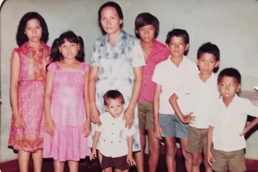 A slightly blurred, grainy colour photo of one adult woman standing with seven children of varying heights and ages around her.