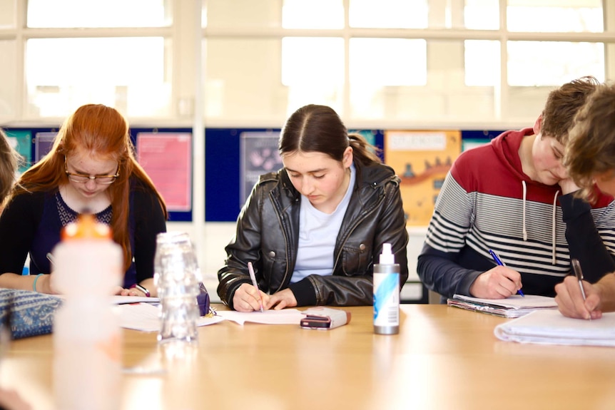 Dickson College students write on paper at a desk.