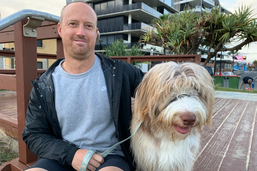 Male dog owner sitting on beach platform with his bordoodle