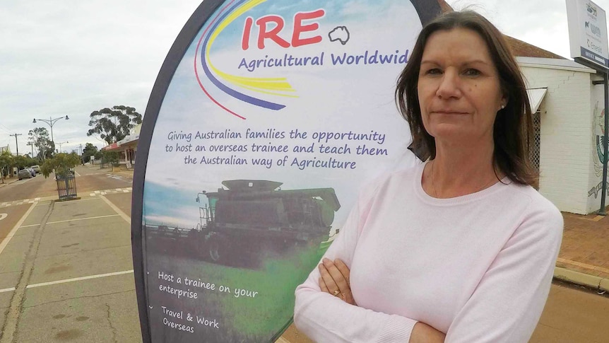 Narelle Vaughn stands in front of a sign advertising her business. The sign is in the median strip of a country road.