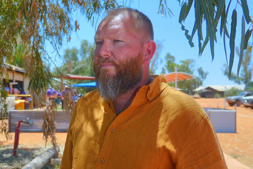 A man wearing a mustard coloured shirt stands under a tree