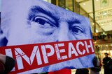 A protestor holds up a sign with Donald Trump's case obscured by the word "Impeach".