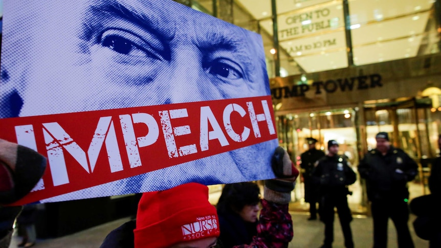 A protestor holds up a sign with Donald Trump's case obscured by the word "Impeach".