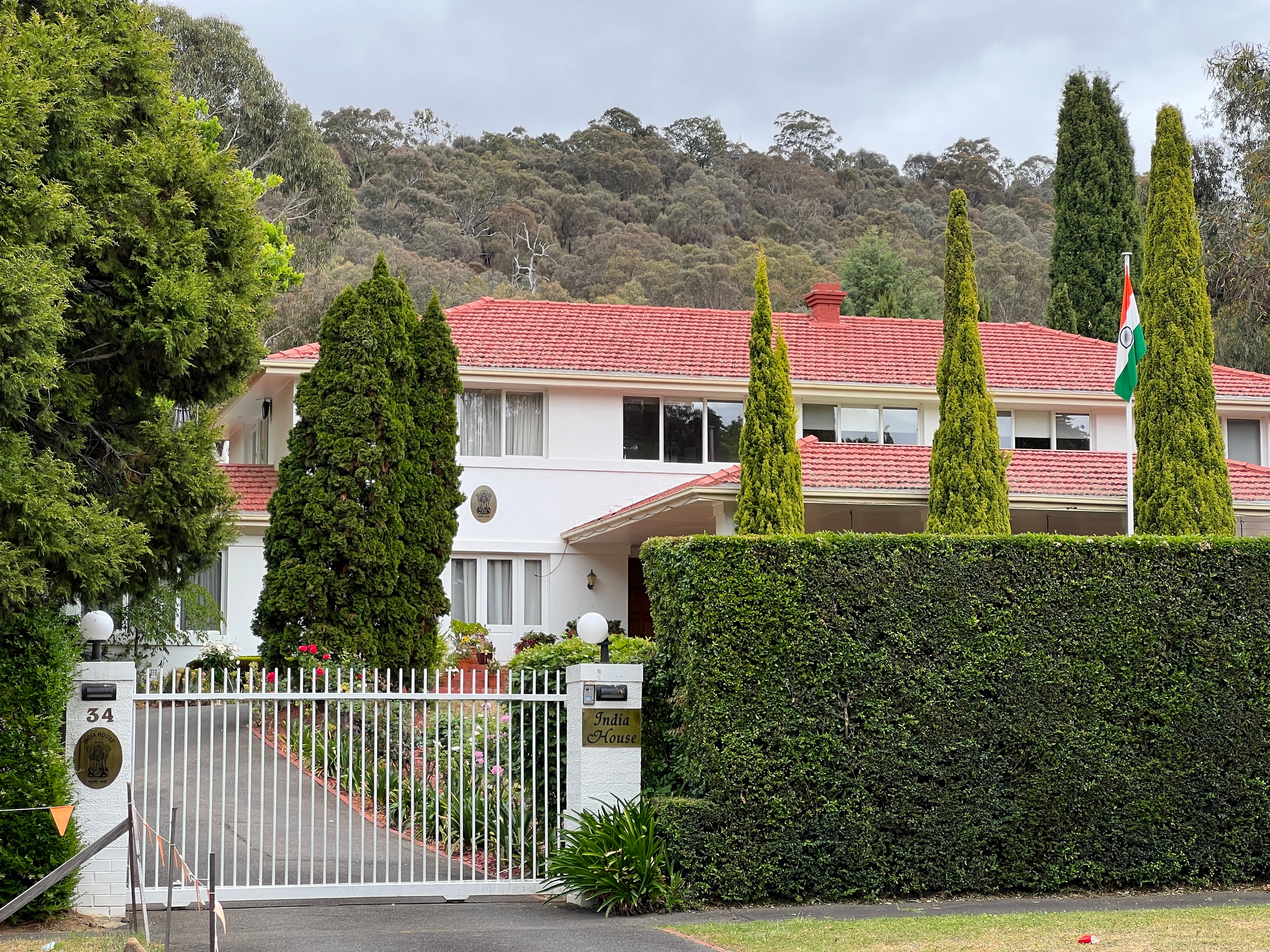A large white house with red tiled roof and Indian flag out the front.