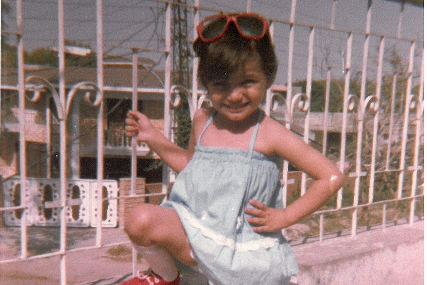 Medium shot of a young girl standing and smiling for the camera.