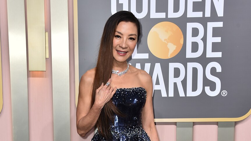 Michelle Yeoh wearing a strapless sparkly dark blue down with two puffy peplums over a long slinky skirt
