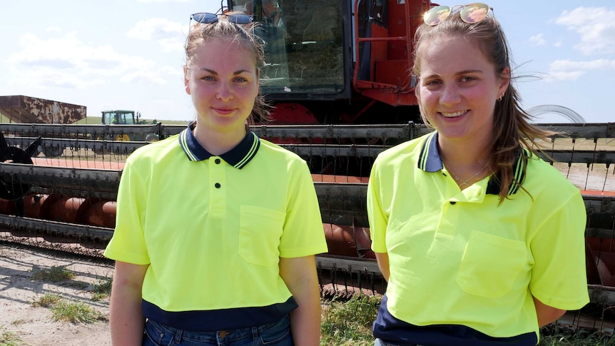 Two young women in hi viz gear stand in front of a tractor.