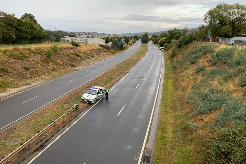 An empty Highway with a lone police car and officer standing outside.