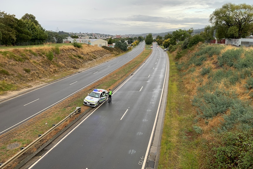 An empty Highway with a lone police car and officer standing outside.