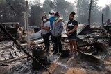 A man and three women, all wearing masks, stand in the ruins of a burnt out house in Oregon.