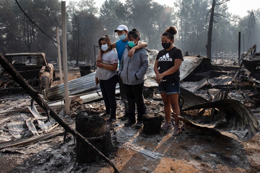 A man and three women, all wearing masks, stand in the ruins of a burnt out house in Oregon.
