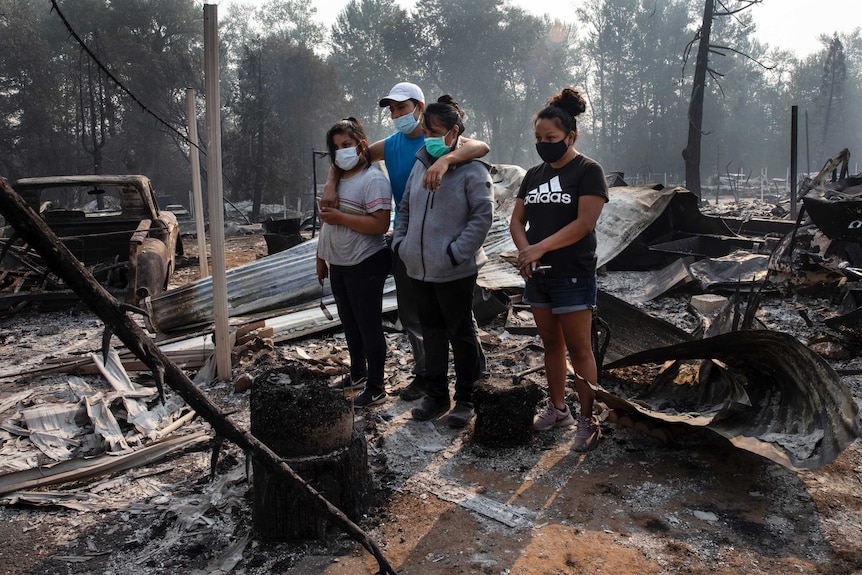 A man and three women, all wearing masks, stand in the ruins of a burnt out house in Oregon.