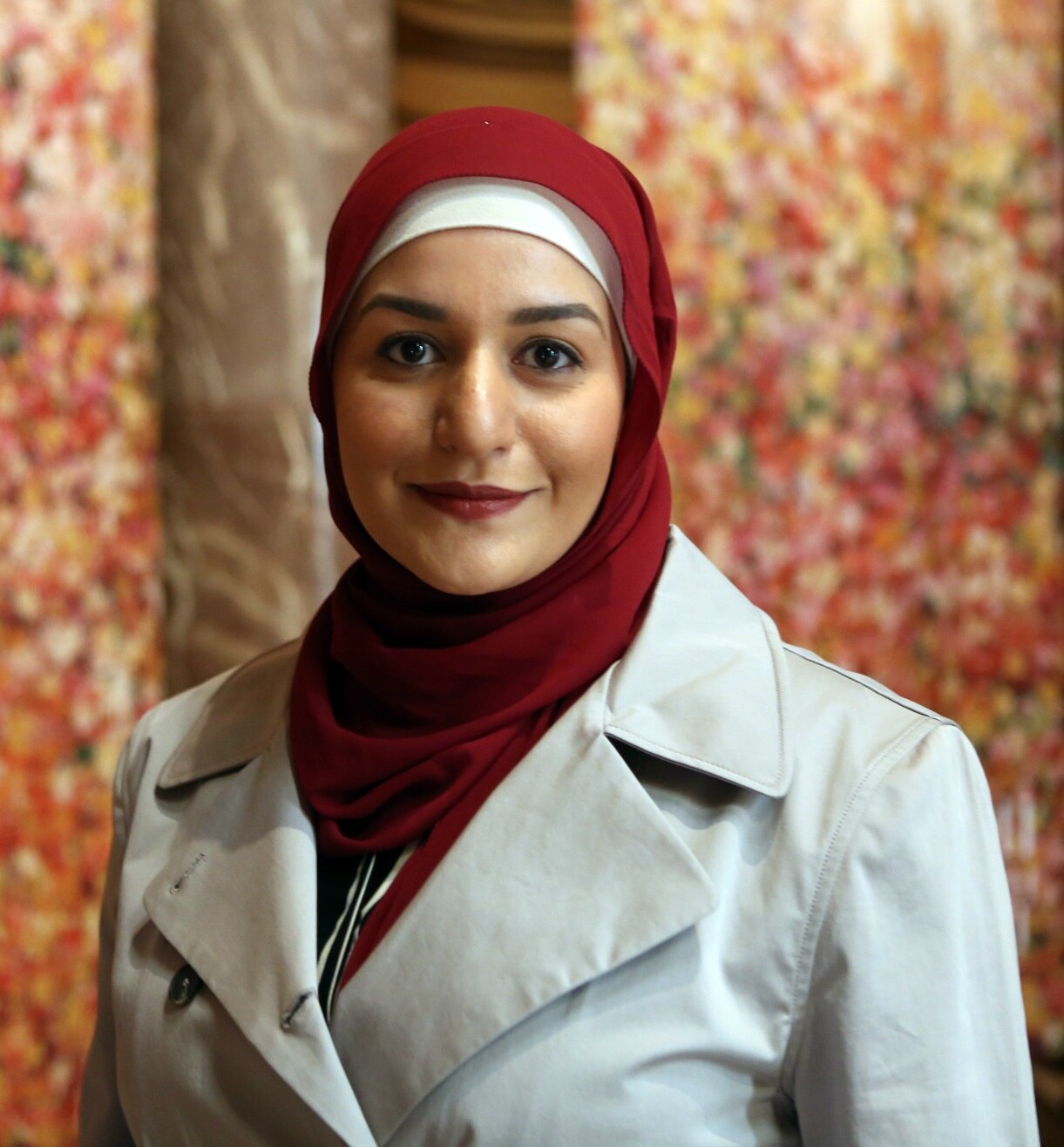 A close up photo of Amani Haydar wearing a red hijab and fawn coat