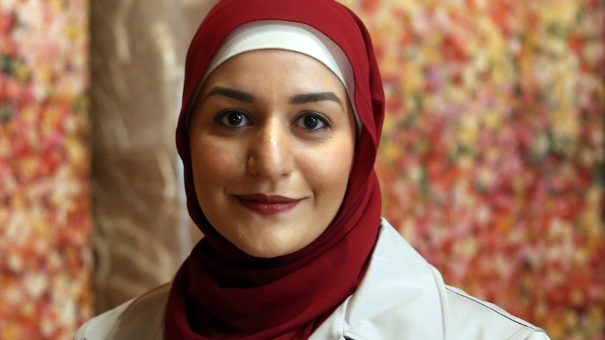 A close up photo of Amani Haydar wearing a red hijab and fawn coat