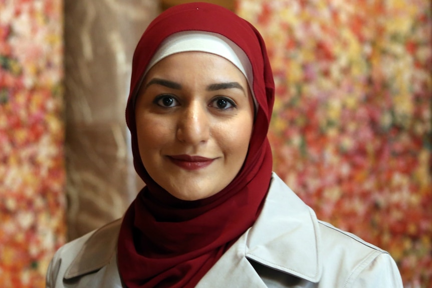 A close up photo of Amani Haydar wearing a red hijab and fawn coat