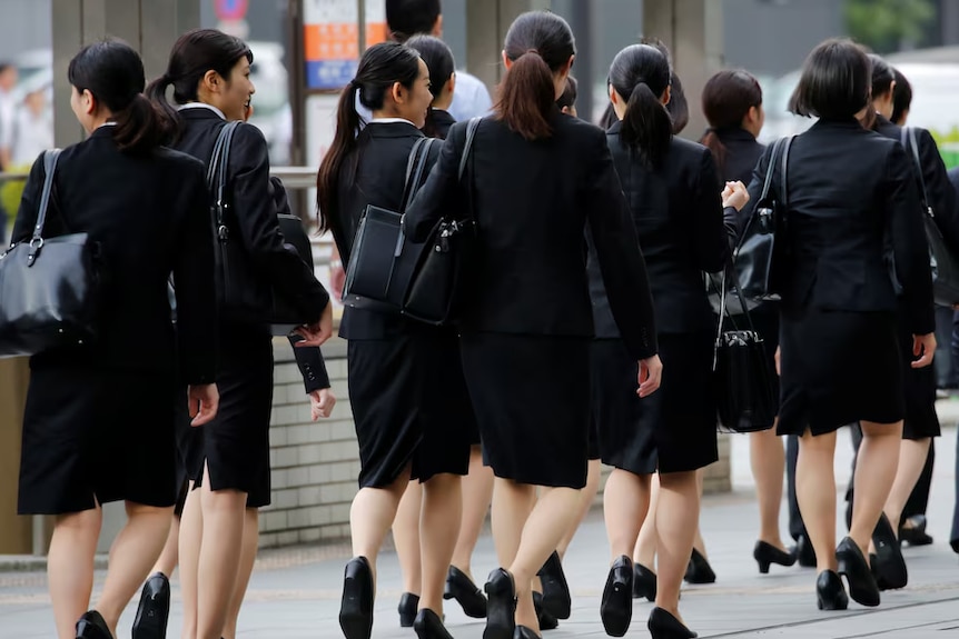 A group of women wearing black office clothing and heels walking in the city
