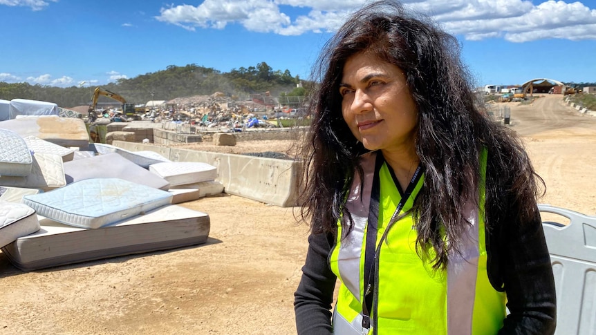 A woman with long dark hair wears a hi-vis safety vests at an outdoor recycling site