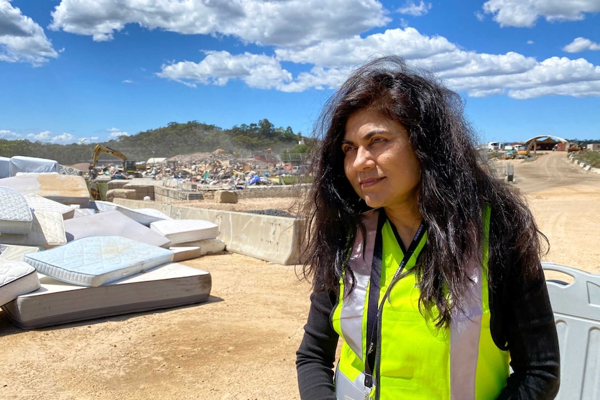 A woman with long dark hair wears a hi-vis safety vests at an outdoor recycling site