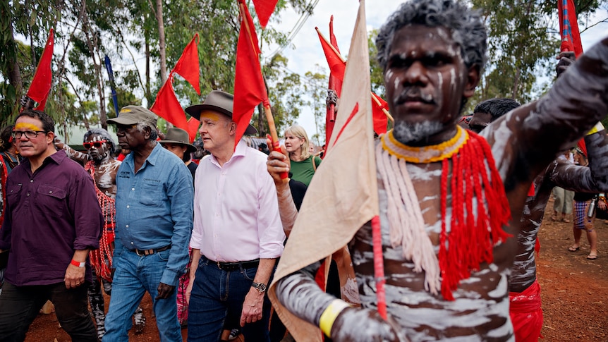 Anthony Albanese walking on a red dirt road surrounded by people in body paint carrying red flags
