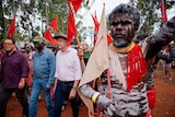 Anthony Albanese walking on a red dirt road surrounded by people in body paint carrying red flags