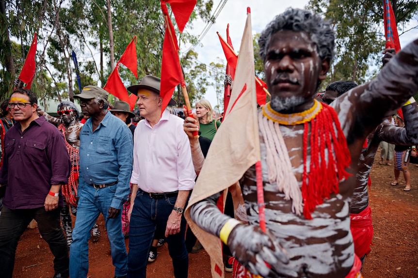 Anthony Albanese walking on a red dirt road surrounded by people in body paint carrying red flags