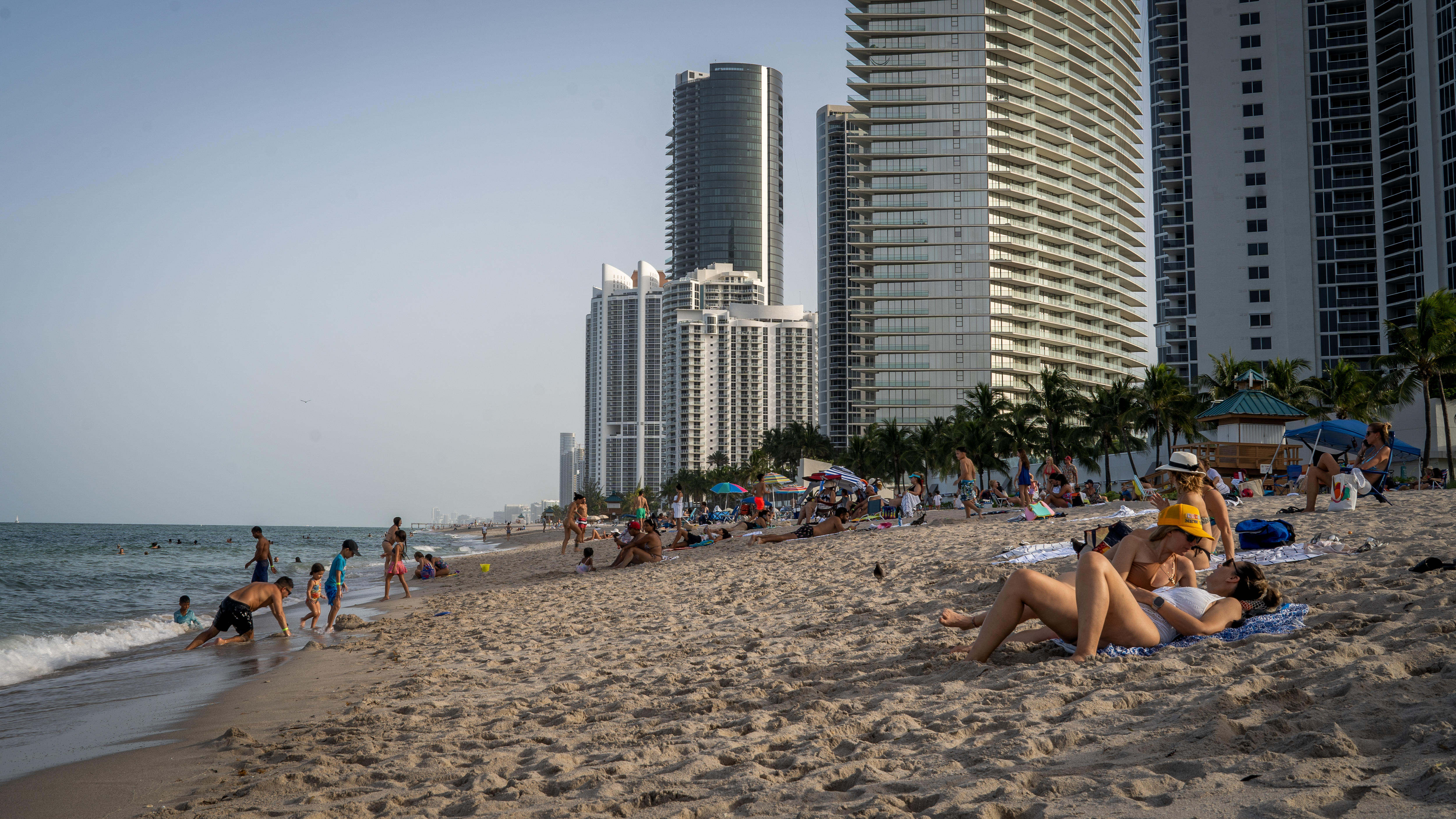 People lounge on a beach with tall skyscrapers in the background