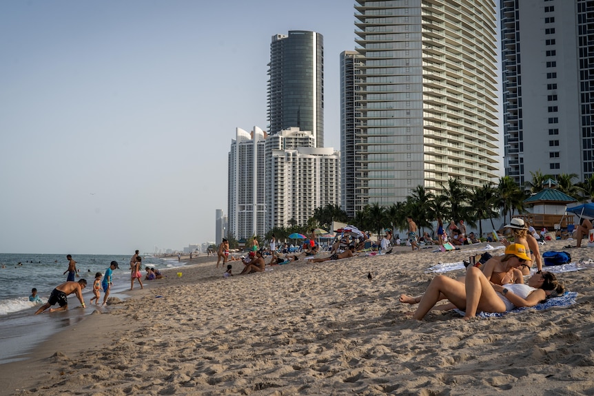 People lounge on a beach with tall skyscrapers in the background