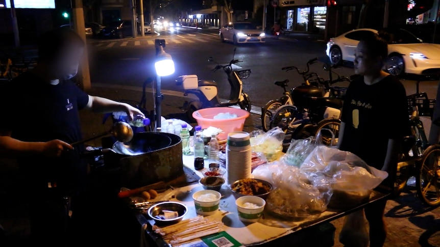 A photo taken at night of an unidentified street food vendor serving a customer.