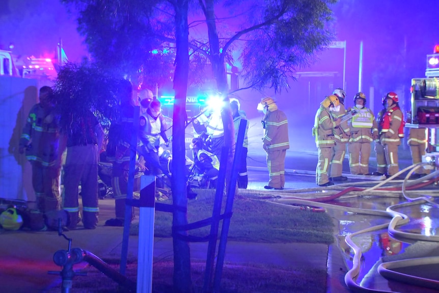 More than a dozen firefighters illuminated by emergency lights at night.