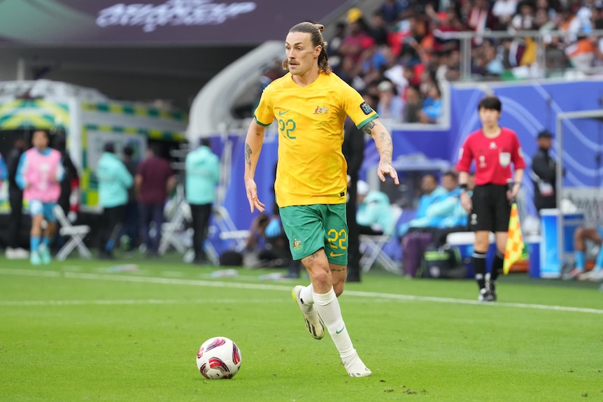 A soccer player wearing yellow and green dribbles the ball during a game