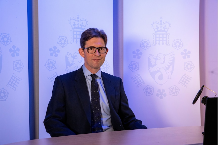 Man in suit and glasses sits at table.