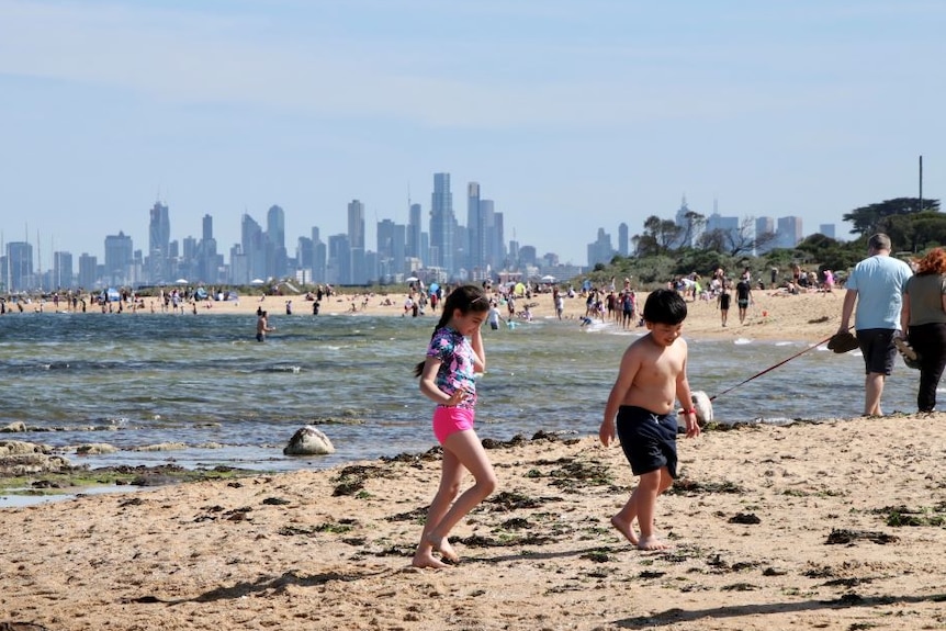 A young girl and boy play on a beach with the Melbourne city skyline in the distance.