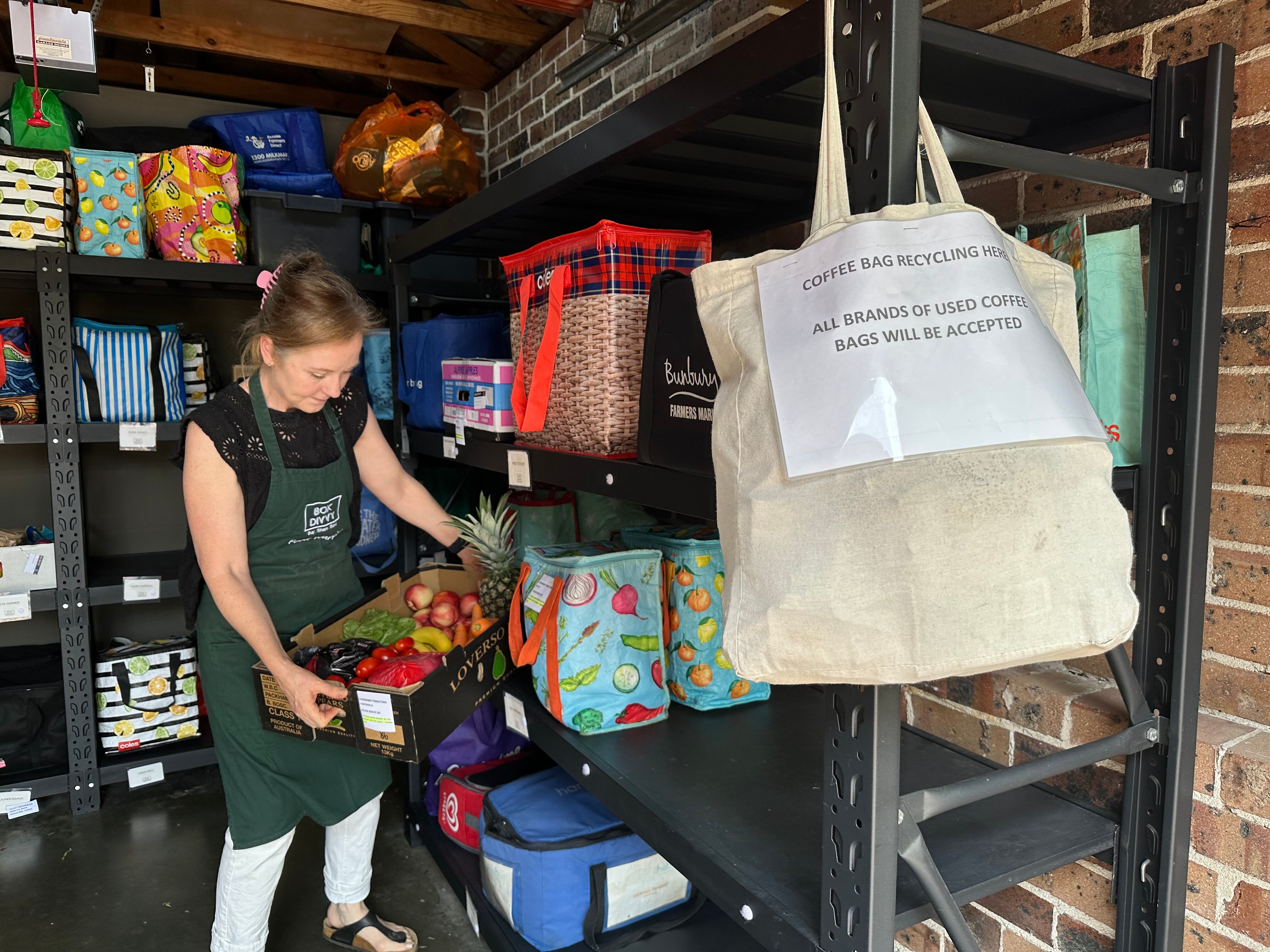 Una mujer recoge una caja de verduras de un estante en un garaje. 