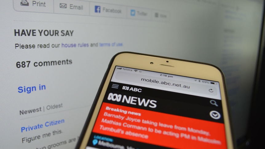 ABC News on mobile phone with comments page on computer screen in background.