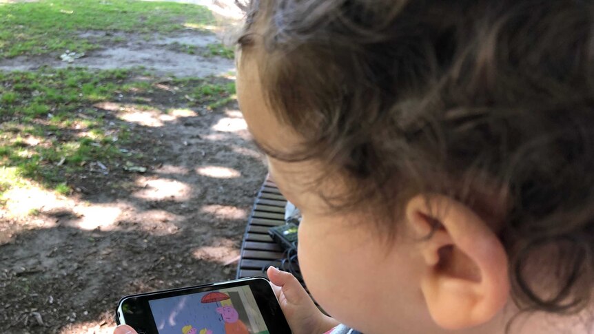 A toddler watches a children's television program using an app on his father's phone.