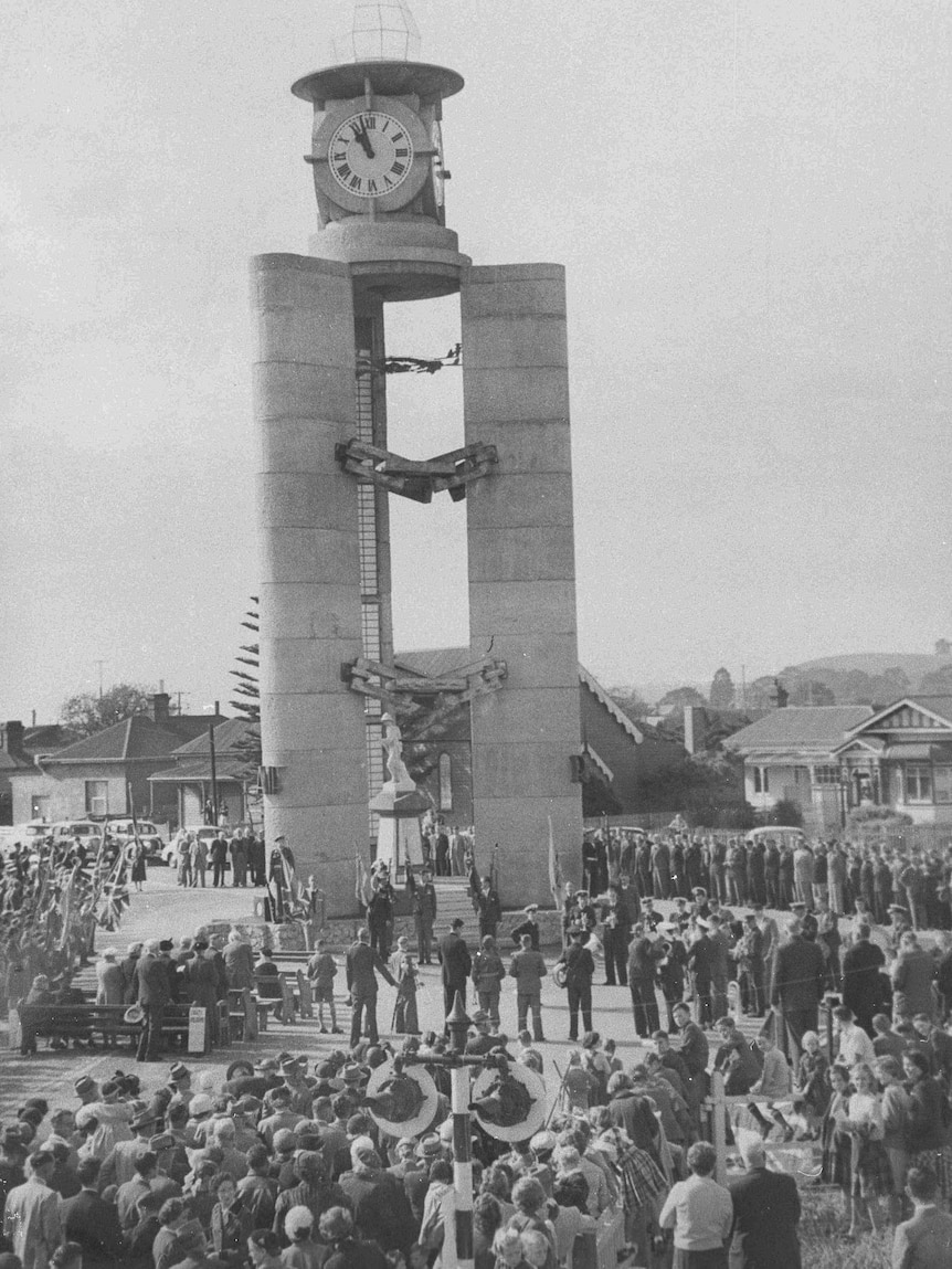 Old monochrome image of a large crowd gathered for formal ceremony around the base of large clock tower.