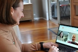 A woman smiles as she looks at a laptop on a table. She is video calling a man through a web browser telehealth program.