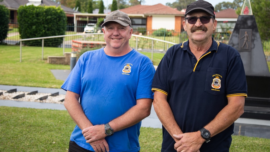 two men standing wearing caps and smiling