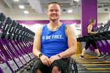 A smiling man sits in a wheelchair between treadmills