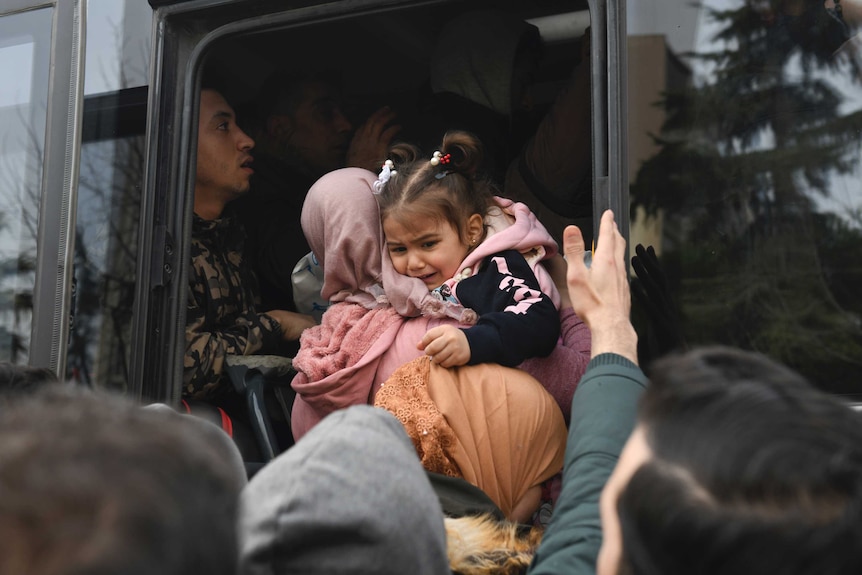 A little girl cries in her mother's arms as the family fight through crowds to board a bus.