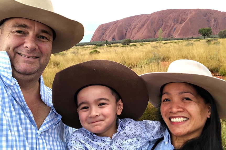A man, his young son and wife pose for a selfie in front of Uluru