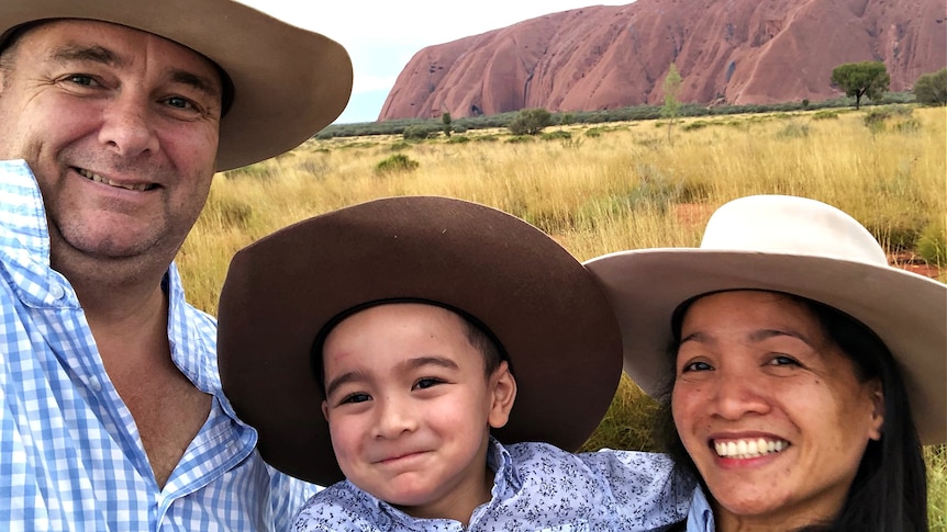 A man, his young son and wife pose for a selfie in front of Uluru