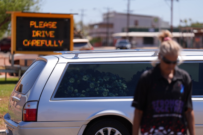 A person stands next to hearse on the street.