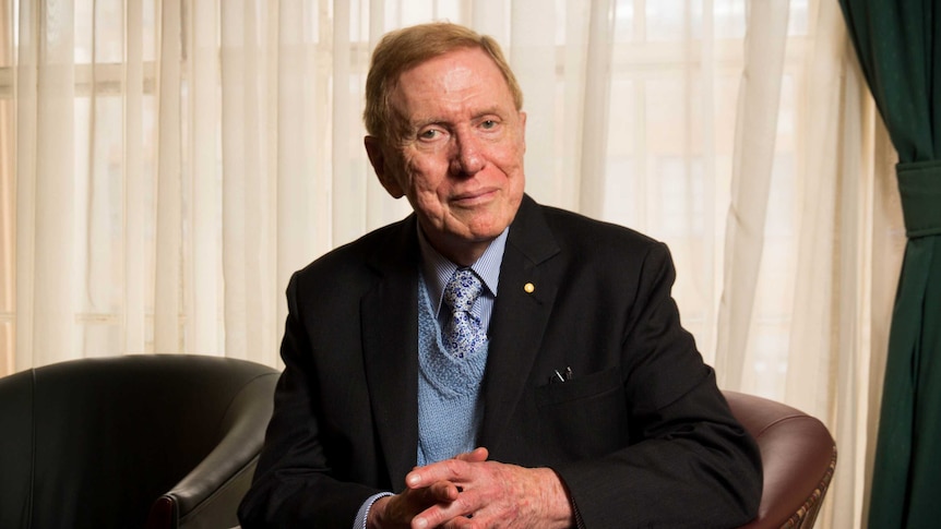 The Hon. Michael Kirby sits in a chair in front of a curtained window.