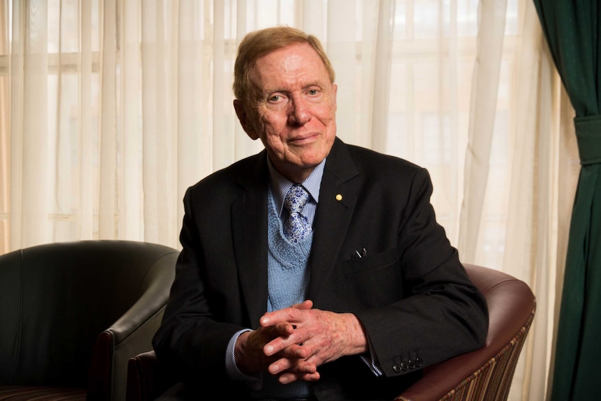 The Hon. Michael Kirby sits in a chair in front of a curtained window.