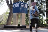 Woman in headscarf passes in front of QUT sign