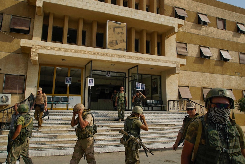 Russian military police soldiers walk outside a hospital in Deir el-Zor. The building has a faded photo of Assad on the front.