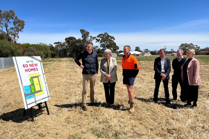 Two women and four men stand on grass with a sign saying up to 60 homes